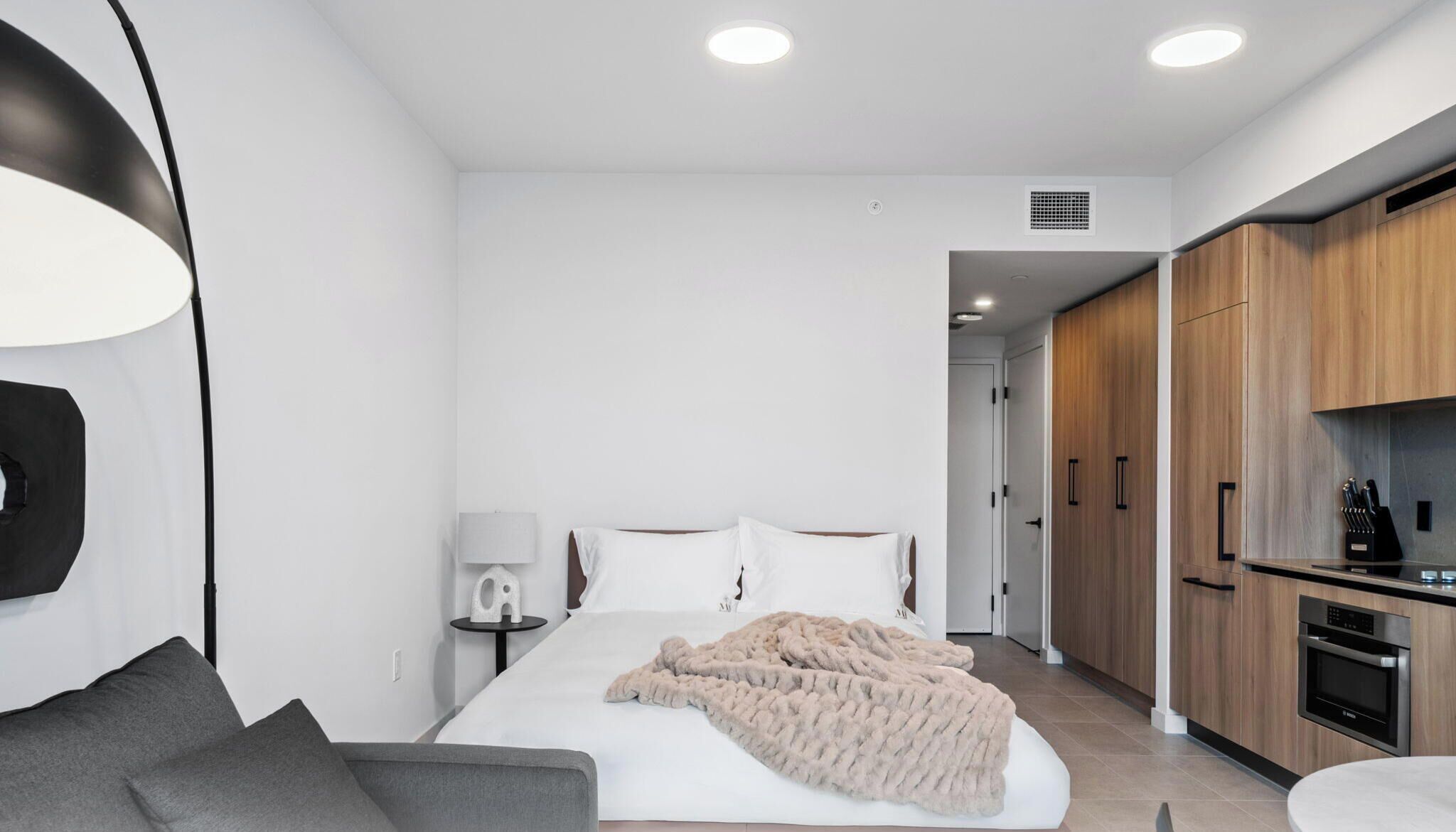 Une chambre d’hôtel moderne équipée d’un lit, d’une table de chevet, d’une lampe et d’une kitchenette.