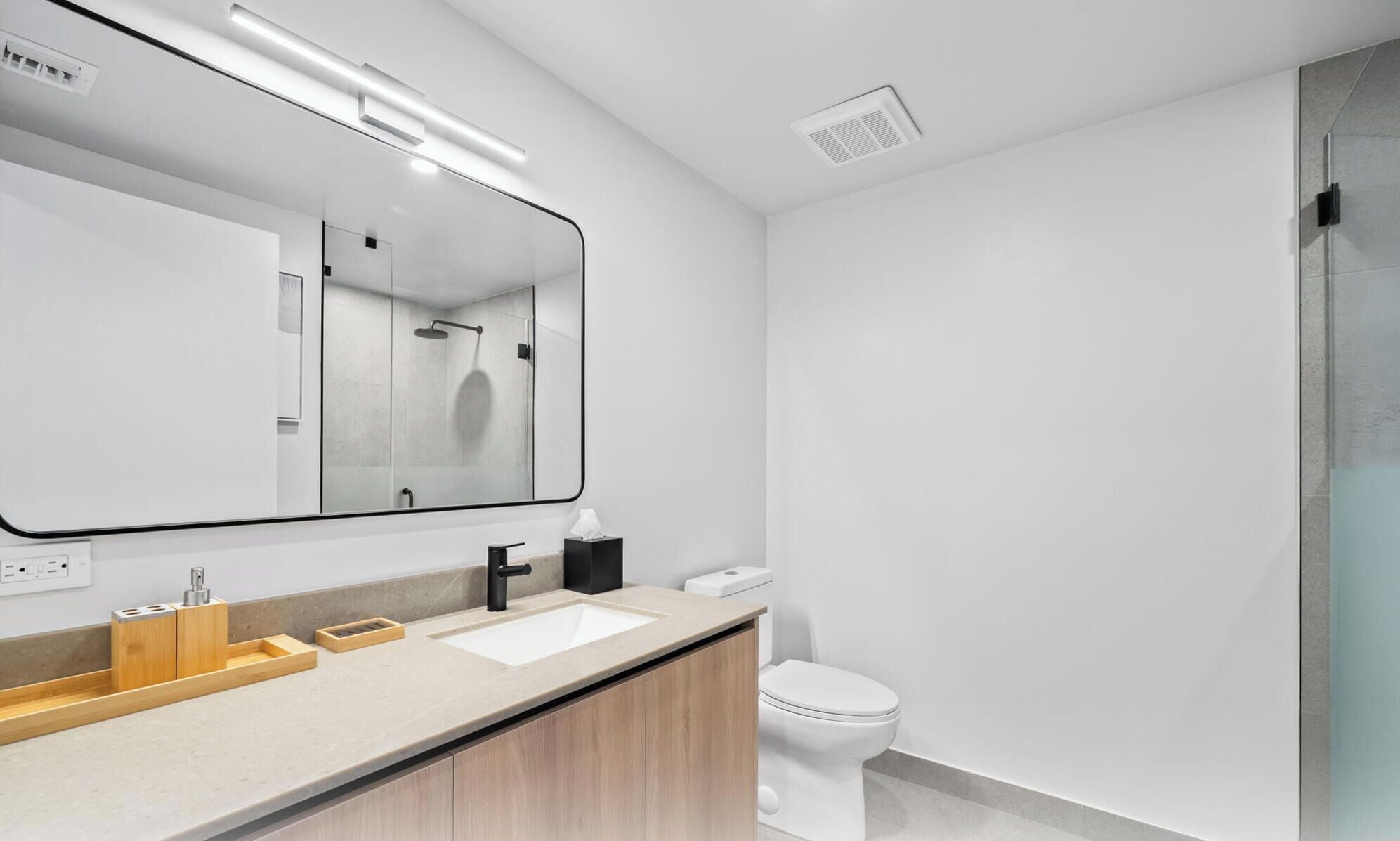 Un baño moderno con un espejo grande, un lavamanos, un inodoro y una zona de ducha.