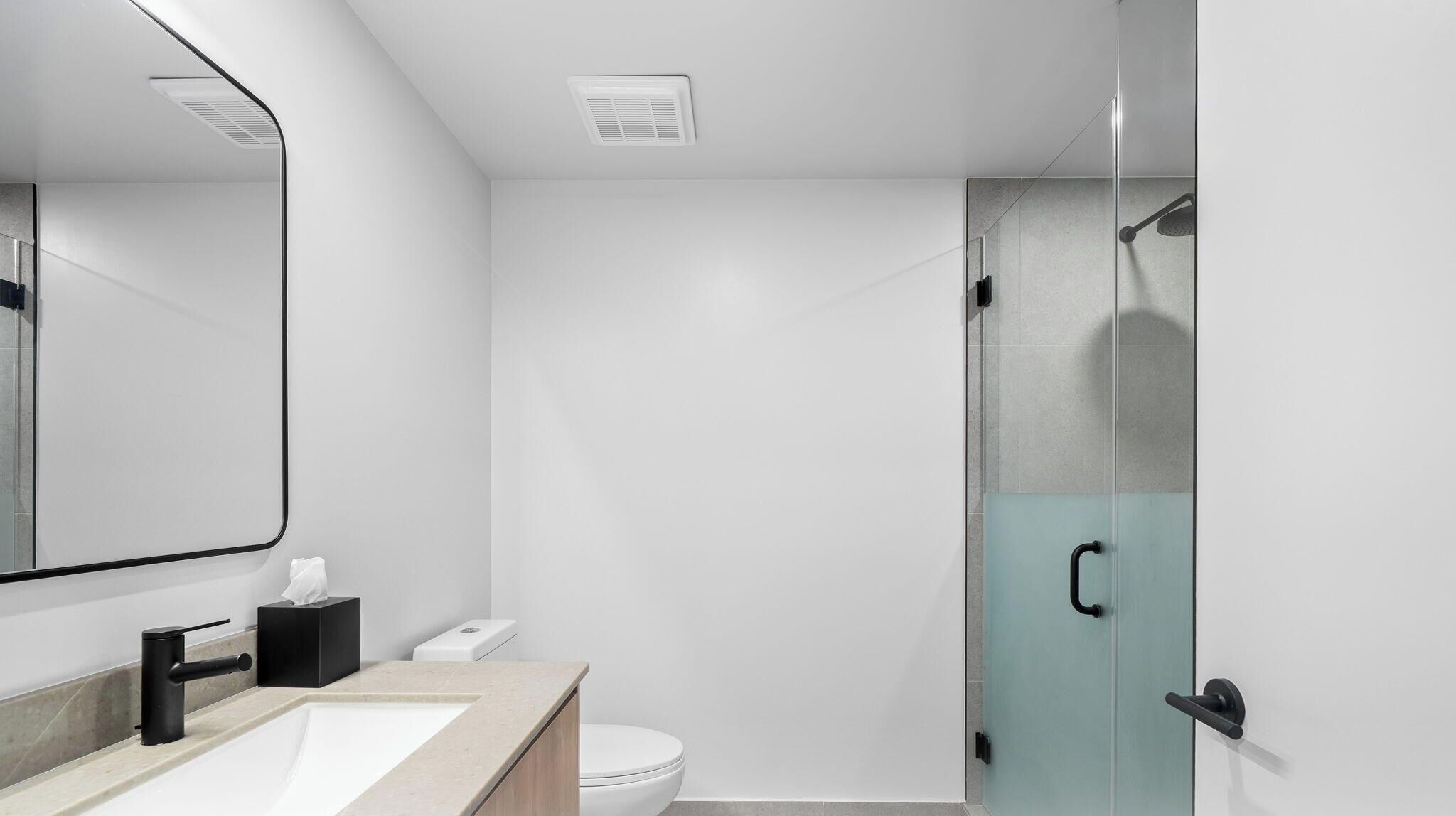 Un bany modern amb un lavabo, vàter i plat de dutxa amb envàs de vidre.