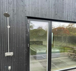A modern building with a large sliding glass door, a metal showerhead, and a wooden fence in the background.