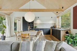 Una cocina moderna con una isla grande, vigas de madera en el techo y vistas a la vegetación.