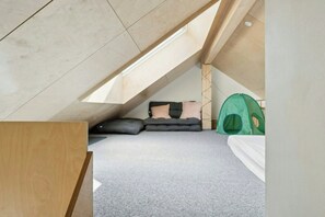 A loft bedroom with a sloped ceiling, a green tent-like structure, and a grey carpet.