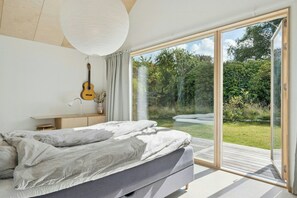 A bedroom with a bed, a guitar, a desk, and a view of a garden through a sliding glass door. - Architectural retreat on North Zealand's coast (Dronningmølle)