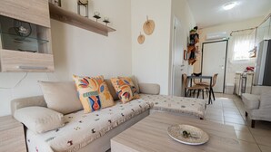 A modern living room with a sectional sofa, a coffee table, and a dining area with chairs and a table. - Chrysanthos Maisonette by RentalsPro - Siviri Halkidiki (Siviri)