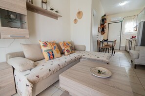 A modern living room with a sectional sofa, a coffee table, and a dining area with chairs and a table. - Chrysanthos Maisonette by RentalsPro - Siviri Halkidiki (Siviri)