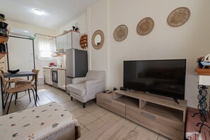 A modern living room with a flat-screen TV, a sofa, a dining table with chairs, a kitchen area, and decorative wall art. - Chrysanthos Maisonette by RentalsPro - Siviri Halkidiki (Siviri)