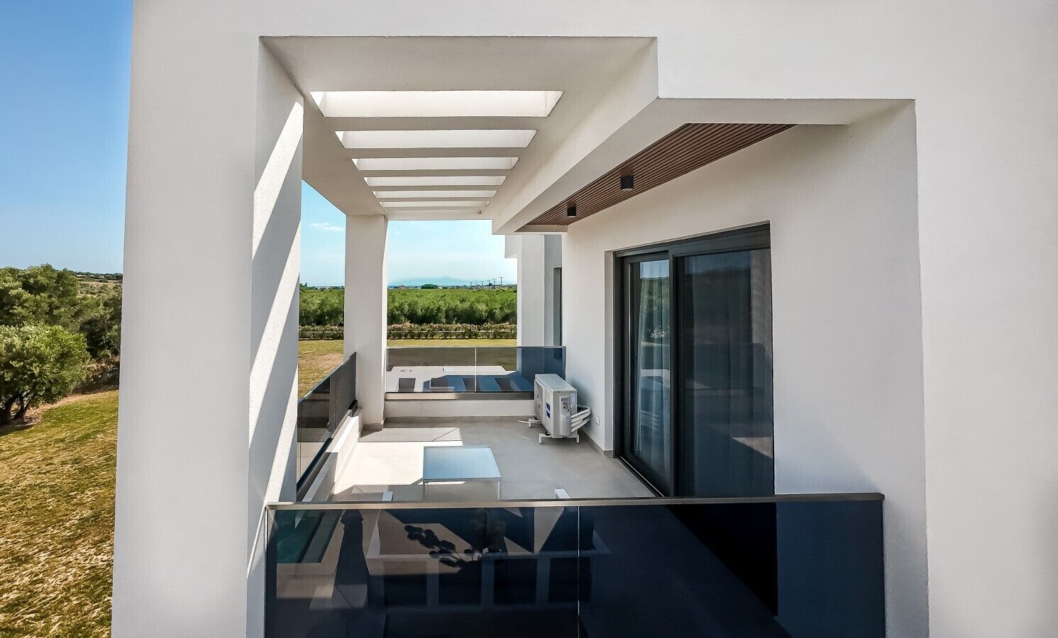 Un balcon moderne avec une balustrade en verre, un petit coin salon et une vue sur la campagne.