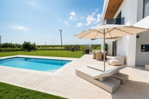 Un espace piscine extérieur moderne, doté d’une terrasse en bois, de chaises longues et d’une pergola avec un parasol.