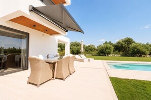 Une terrasse extérieure moderne, avec des meubles en osier, une table en verre et une piscine.
