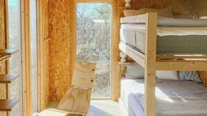 Interior de madera con literas, una silla plegable y un ventanal grande.