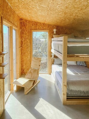 A wooden interior with bunk beds, a fold-out chair, and a large window. - Nature and veranda in perfect alignment (Djurhamn)