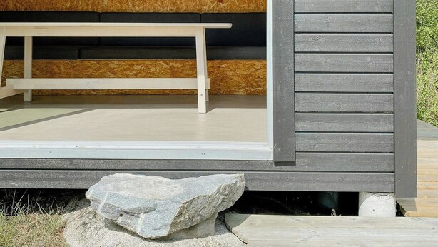 Una cabaña moderna con interior de madera, un banco y un ventanal pequeño.