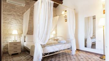 Un letto a baldacchino con tenda, un comodino con una lampada, uno specchio e un muro in pietra.