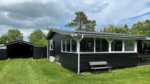 A black wooden cabin with a covered porch, a garage, and a grassy yard. - Charm and idyll in Hou (Hals)