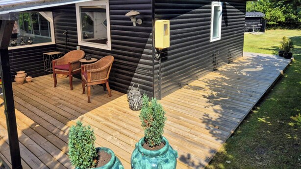 A log cabin with a deck, wicker chairs, a table, and two potted plants. - Charm and idyll in Hou (Hals)