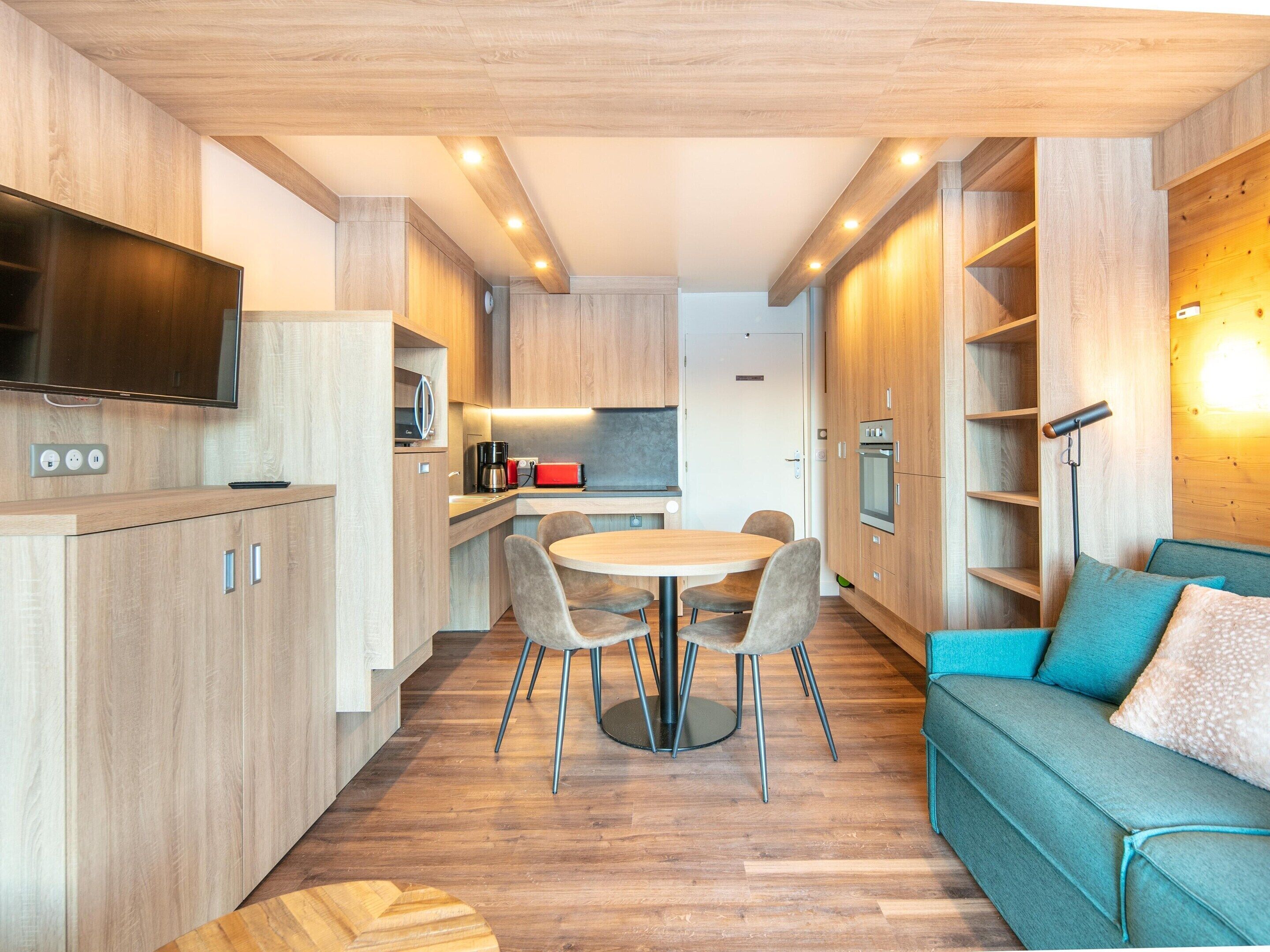 Una cocina moderna con armarios de madera, una mesa de comedor con sillas, un horno empotrado y un televisor de pantalla plana.