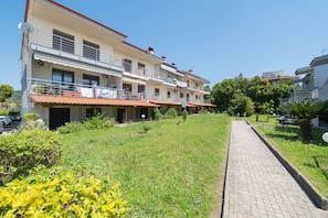 A multi-story building with balconies, a paved pathway, and surrounding greenery. - Ammos Premium Apartment by RentalsPro - Fourka Halkidiki (Fourka)
