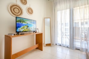 A modern living room with a flat-screen TV on a wooden console, a large mirror, and a view of the outdoors through sheer curtains. - Ammos Premium Apartment by RentalsPro - Fourka Halkidiki (Fourka)