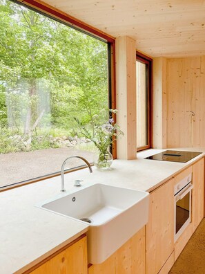 Eine moderne Küche mit großem Fenster, Holzschränken, einer weißen Spüle und einem eingebauten Backofen.