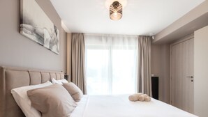 Een hotelkamer met een groot bed, een schilderij aan de muur, een plafondlamp en uitzicht op het omliggende landschap.