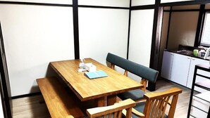 A wooden dining table with benches, a small kitchen area, and a window. - Q stay Toneri Park (Tokyo)