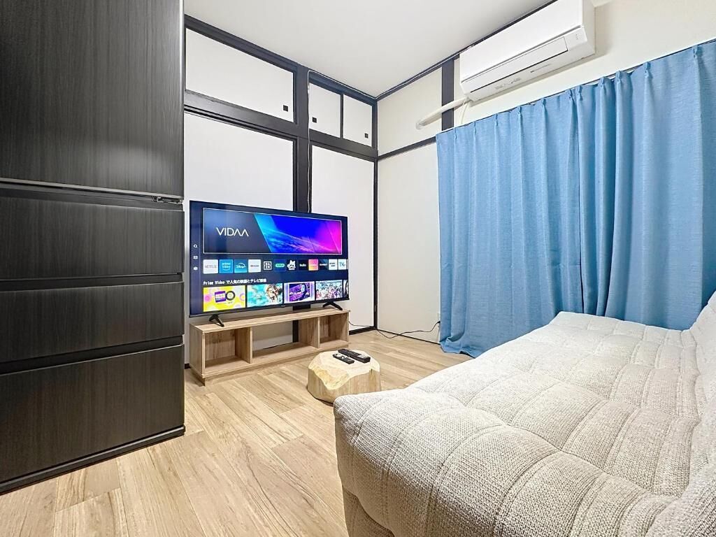 A modern hotel room with a flat-screen TV, wooden flooring, a bed, a wardrobe, and a window with curtains.