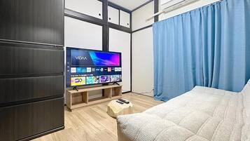 A modern hotel room with a flat-screen TV, wooden flooring, a bed, a wardrobe, and a window with curtains.