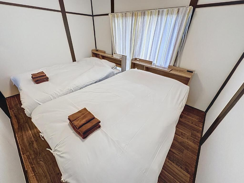 A room with two beds, wooden headboards, a window with curtains, and a wooden floor.