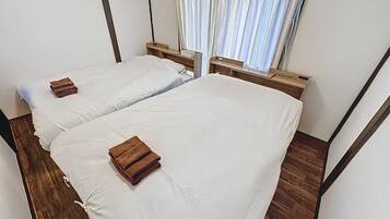 A room with two beds, wooden headboards, a window with curtains, and a wooden floor.
