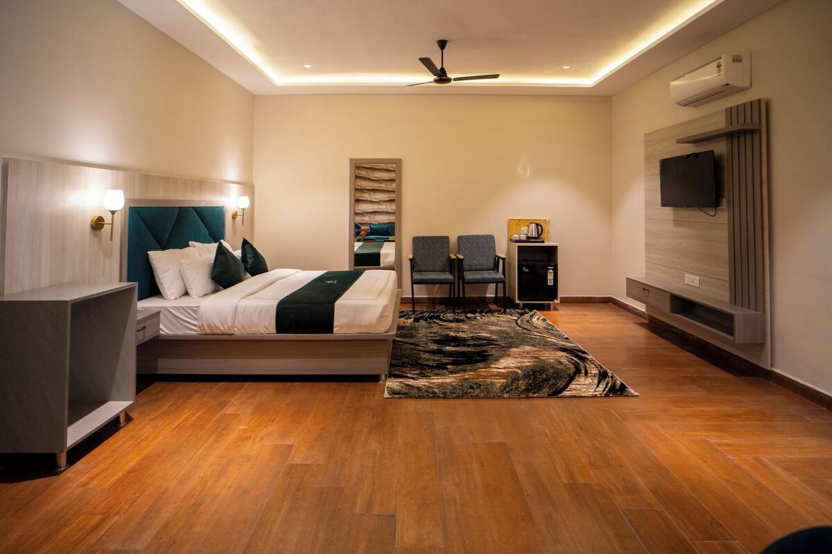 A modern hotel room with a bed, seating area, flat-screen TV, and built-in air conditioning.