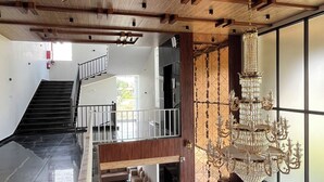 A spacious lobby with a wooden ceiling, a grand chandelier, a staircase, and large windows.