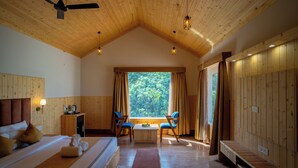 A room with a bed, a desk, two chairs, a window with curtains, and a ceiling fan.