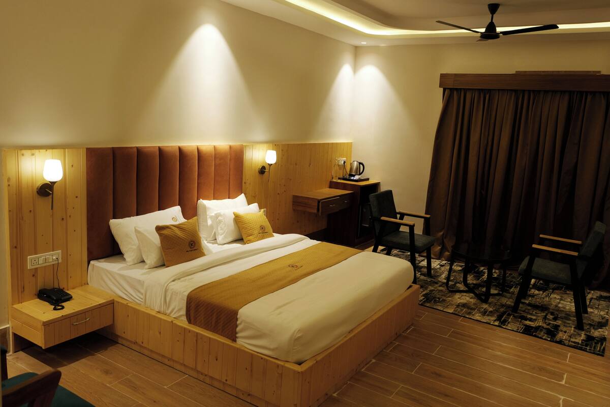 A hotel room with a wooden headboard, a bed with white linens, a desk with a chair, and a ceiling fan.