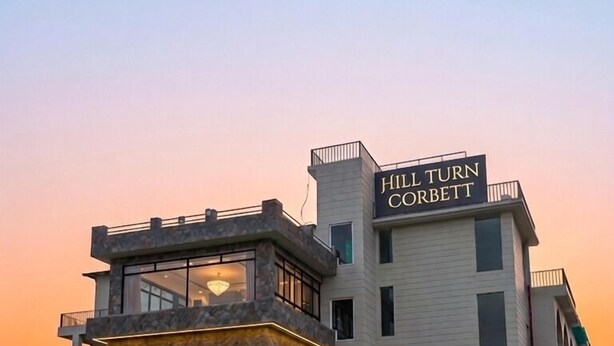 A multi-story hotel with a prominent entrance, a balcony, and a sign reading 'Hill Turn Corbett.'