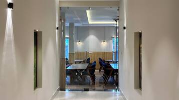 Un pasillo moderno de hotel con suelo de mármol pulido, iluminación empotrada y vista a un comedor con mesas y sillas.