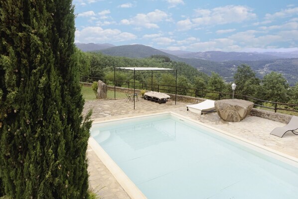 Una piscina con vistas a montañas, rodeada de vegetación y mobiliario exterior.