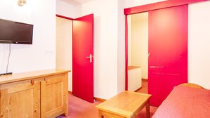 A room with a television, a wooden cabinet, a small table, and red doors. - Cosy Apartment in Modane by Ski-lifts (Modane)