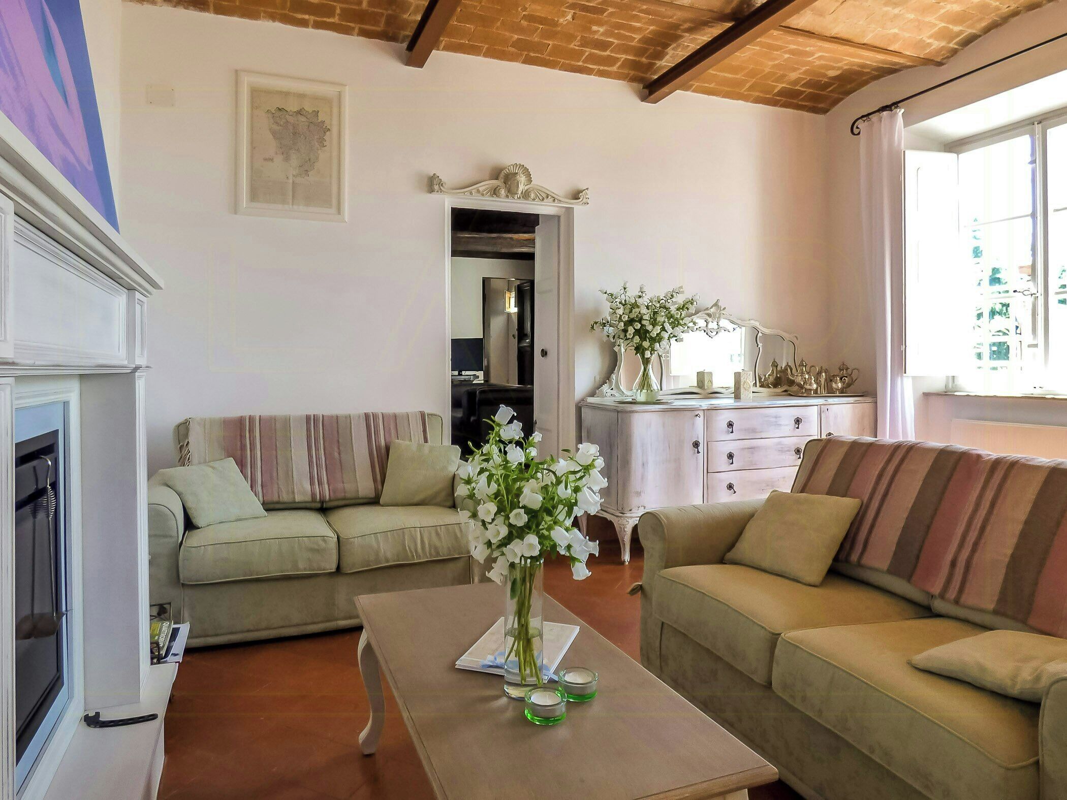 Una sala de estar con chimenea, dos sofás, una mesa de centro con un jarrón de flores, un aparador y un espejo.