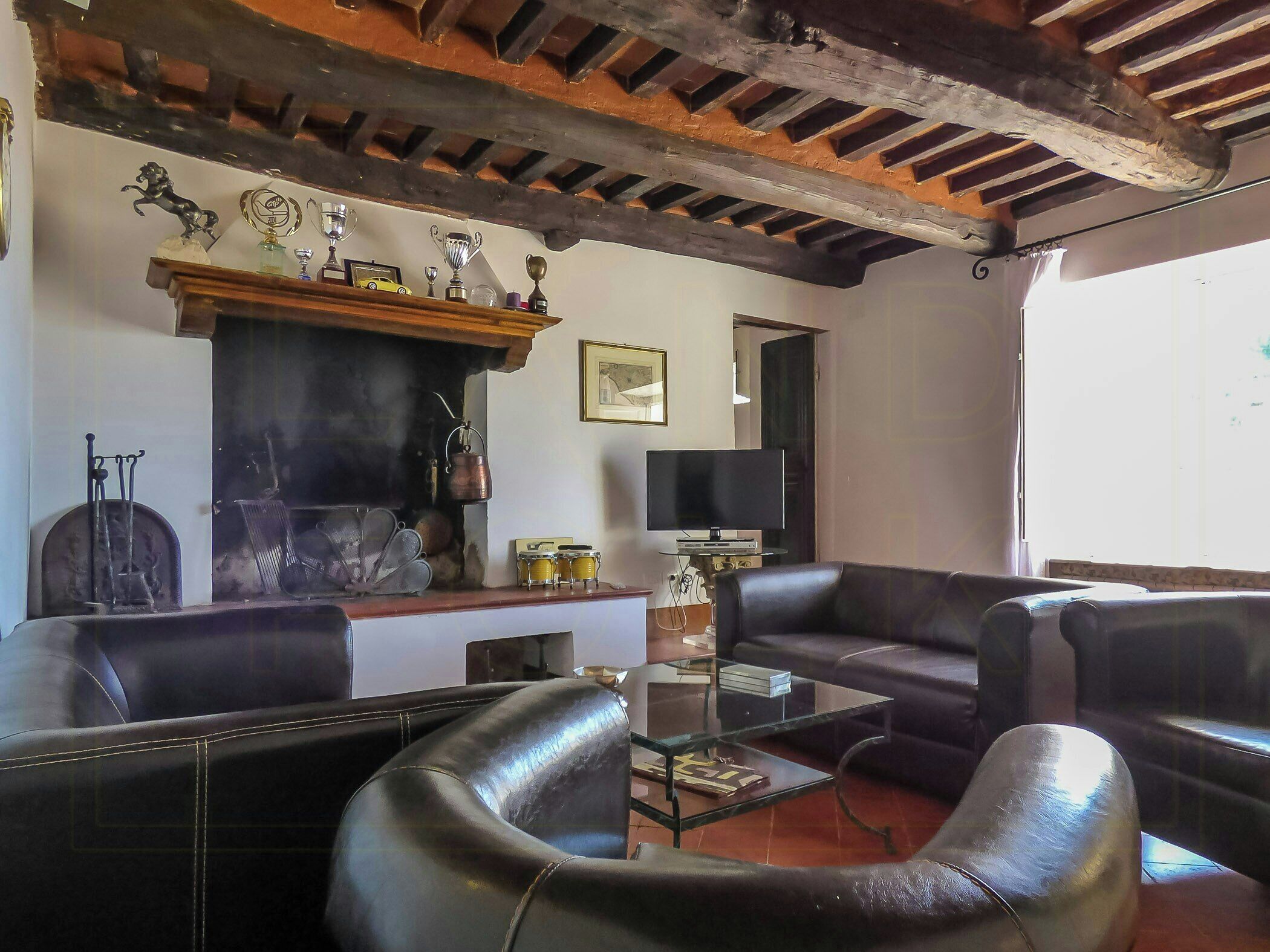 A living room with a fireplace, leather sofas, a glass coffee table, and a television.