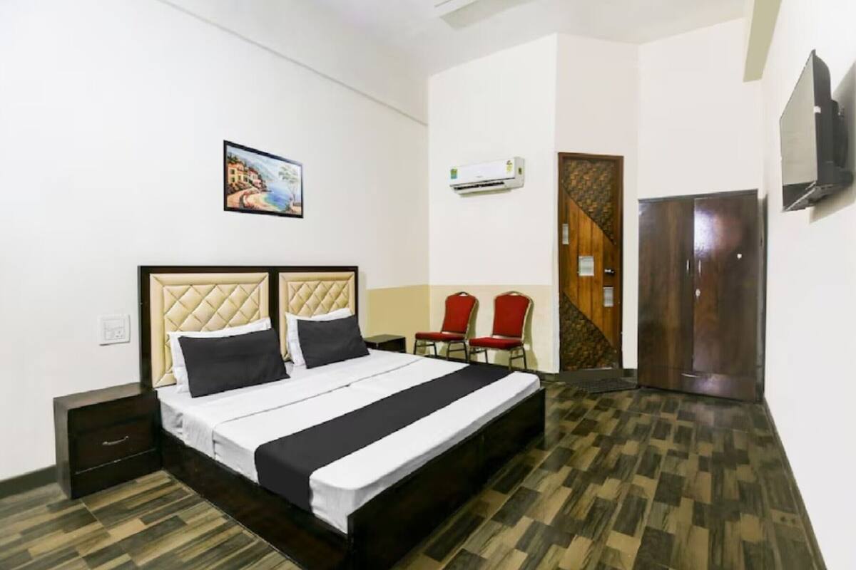 A hotel room with a bed, two chairs, a TV, an air conditioner, and a door.