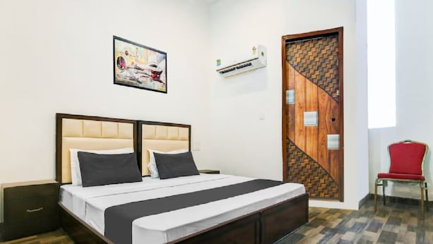 Un dormitorio con una cama, aire acondicionado de pared, una puerta con diseño geométrico y una silla roja.