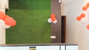 Un área de recepción con una pared de césped artificial verde, un ventilador de techo y un mostrador de recepción.