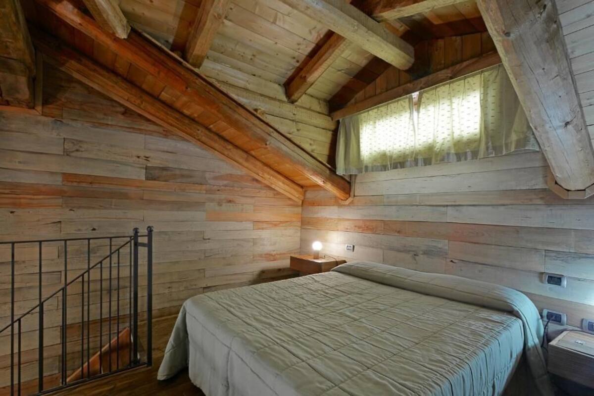 Ein Schlafzimmer in einer Blockhütte mit einem Bett, einem Nachttisch, einem Fenster mit Vorhängen und einer Holztreppe.