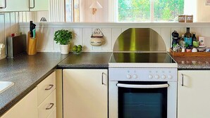 A kitchen with white cabinetry, a Bosch oven, a stainless steel range hood, and a window with a view of greenery. - Summer house by Tranum plantation and beach (Brovst)