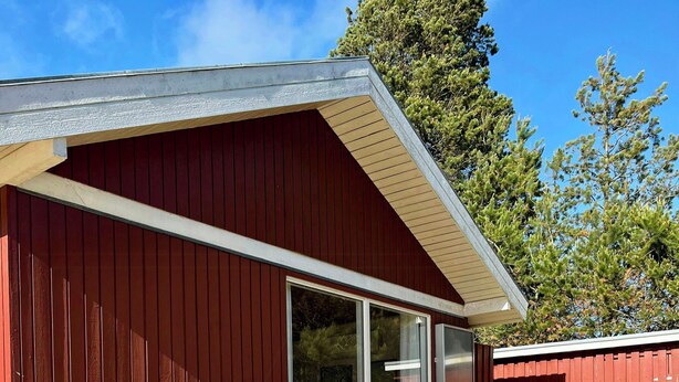 A red building with a wooden deck, two chairs, a table, and a potted plant. - Summer house by Tranum plantation and beach (Brovst)