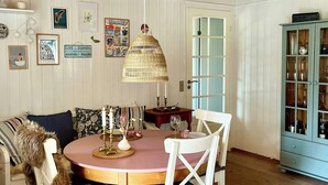 A dining area with a round table, white chairs, a hanging lamp, and a cabinet with glass doors. - Summer house by Tranum plantation and beach (Brovst)