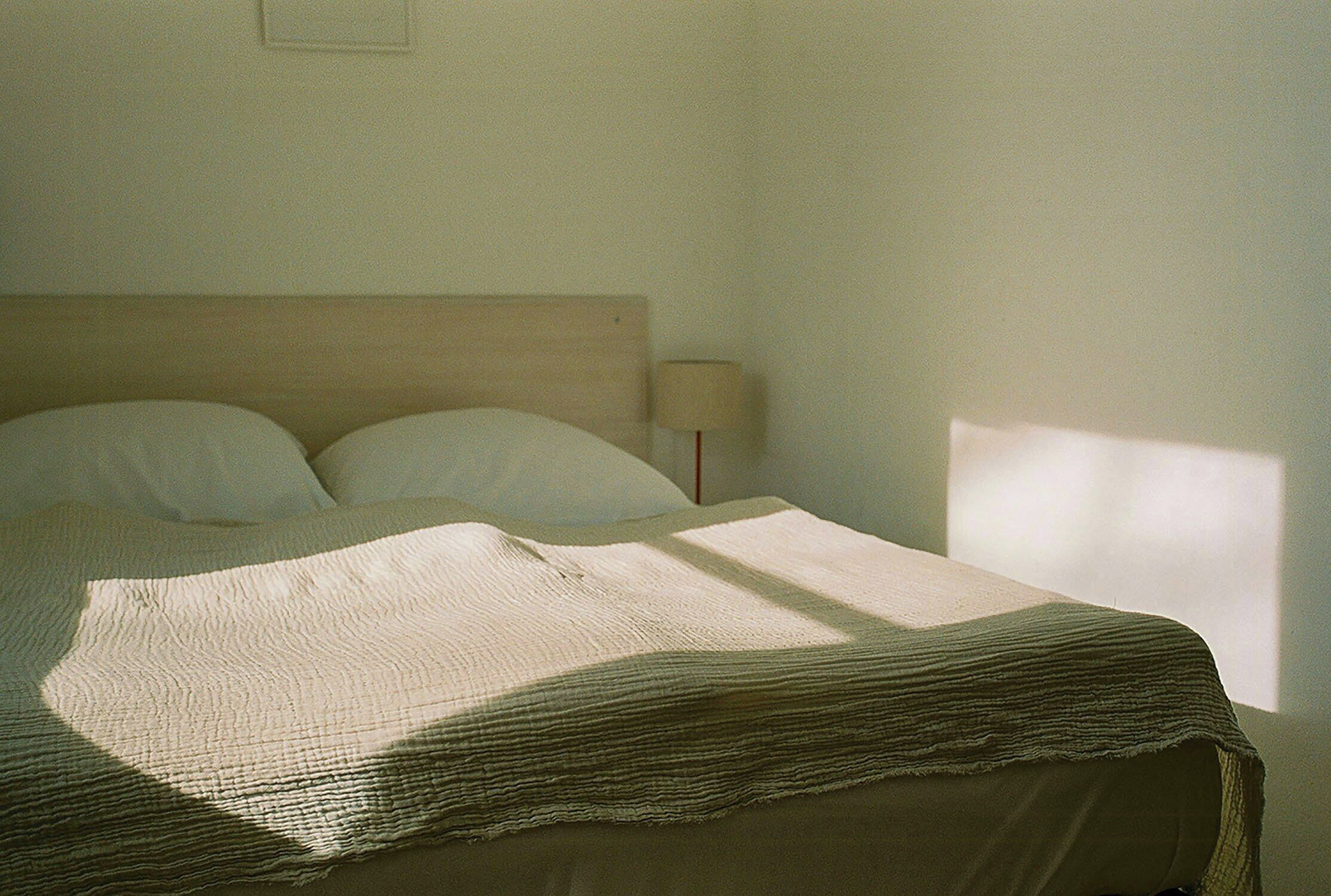 Una cama con cabecera de madera, una lámpara y una ventana que ilumina la cama.
