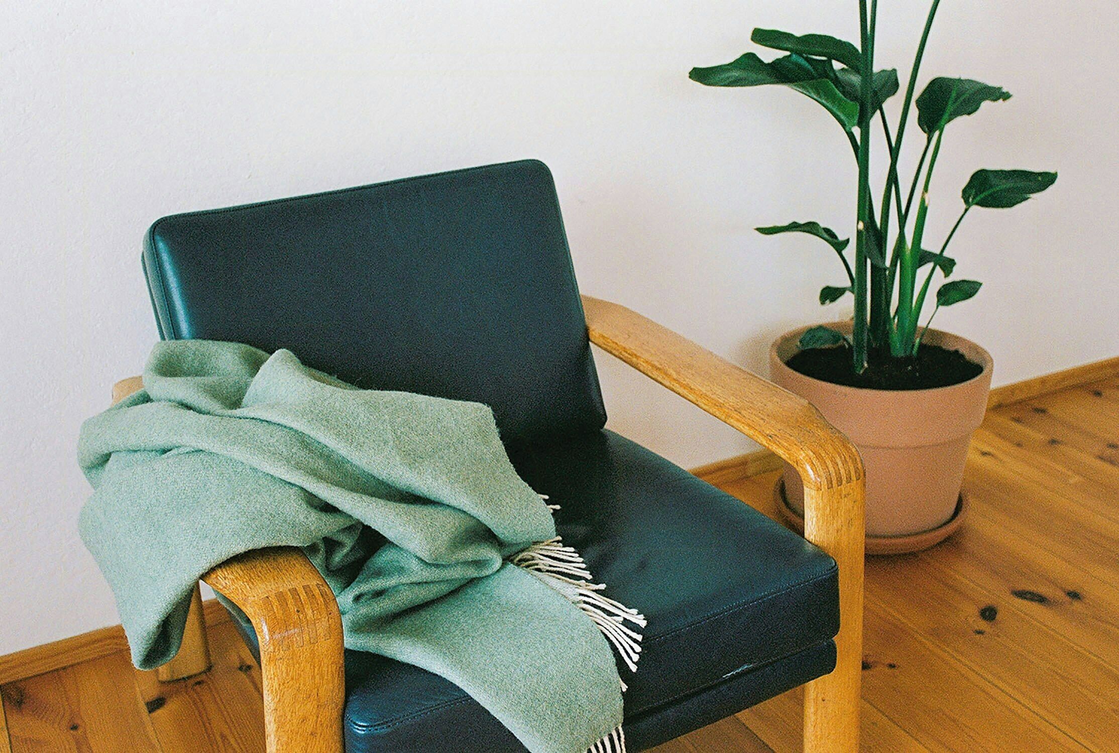 Una silla de madera con un cojín oscuro y una manta verde.