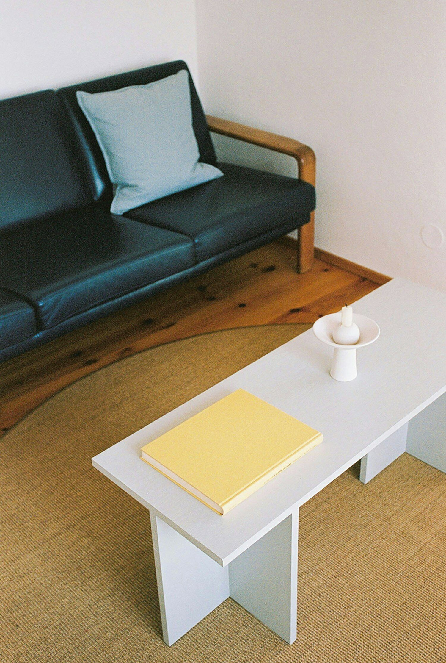 Une pièce avec une table blanche, un livre jaune, une bougie blanche et un canapé bleu foncé agrémenté d’un coussin bleu clair.