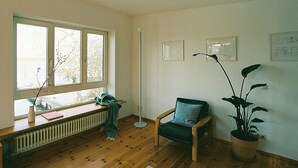 A room with a wooden floor, a window with a view, a chair, a radiator, and a potted plant. - Bauhaus studio with Havel river views in Werder (Werder (Havel))